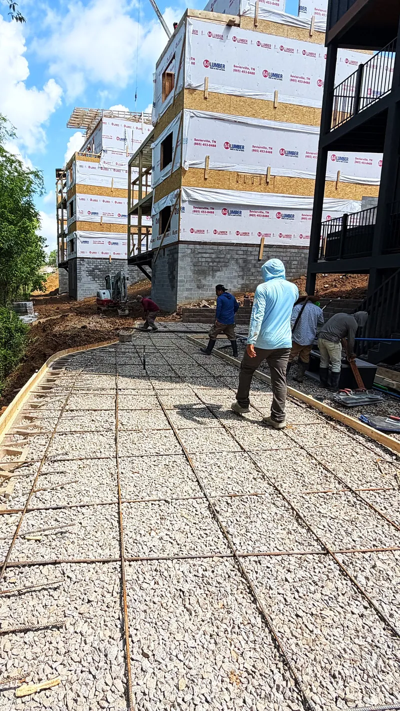 Crew preparing a reinforced concrete walkway on a compacted base at a multi-building site