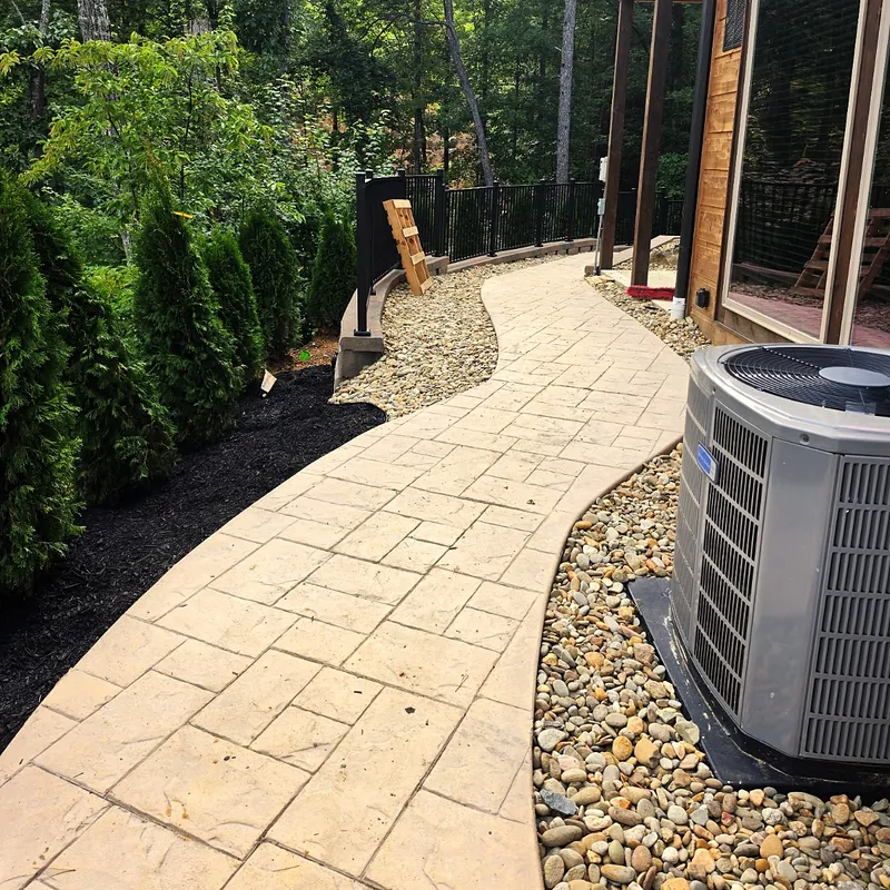 Stamped and colored concrete walkway curving past a cabin, with a river rock border