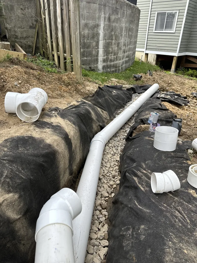 French drain trench lined with filter fabric and drainage gravel, with PVC fittings staged alongside