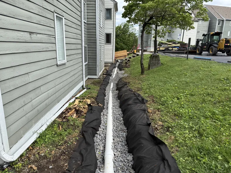 Completed French drain run with filter fabric, gravel and solid pipe tied into the building's downspout
